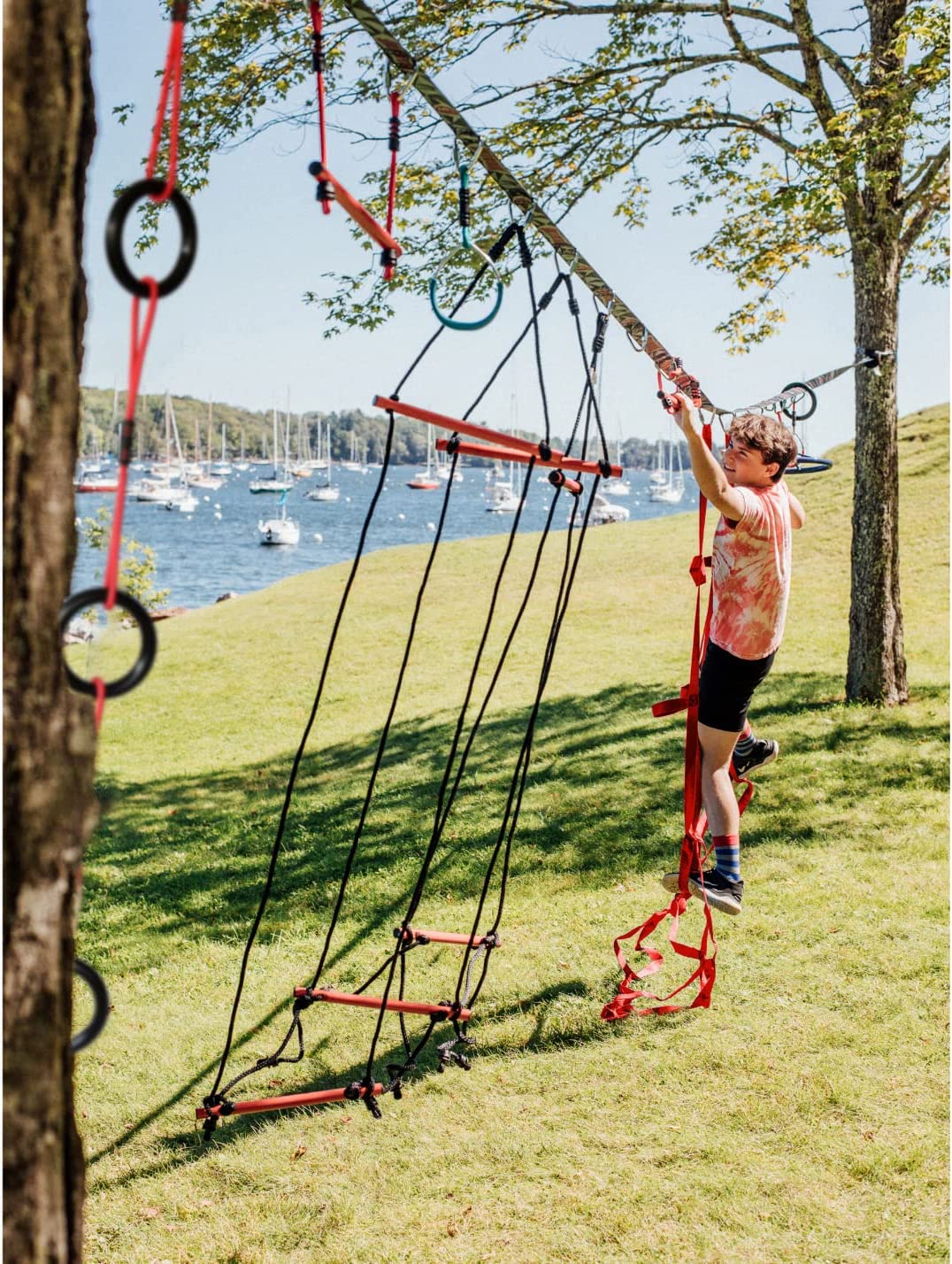 Child playing on a tree swing set with a scenic background of water and trees.
