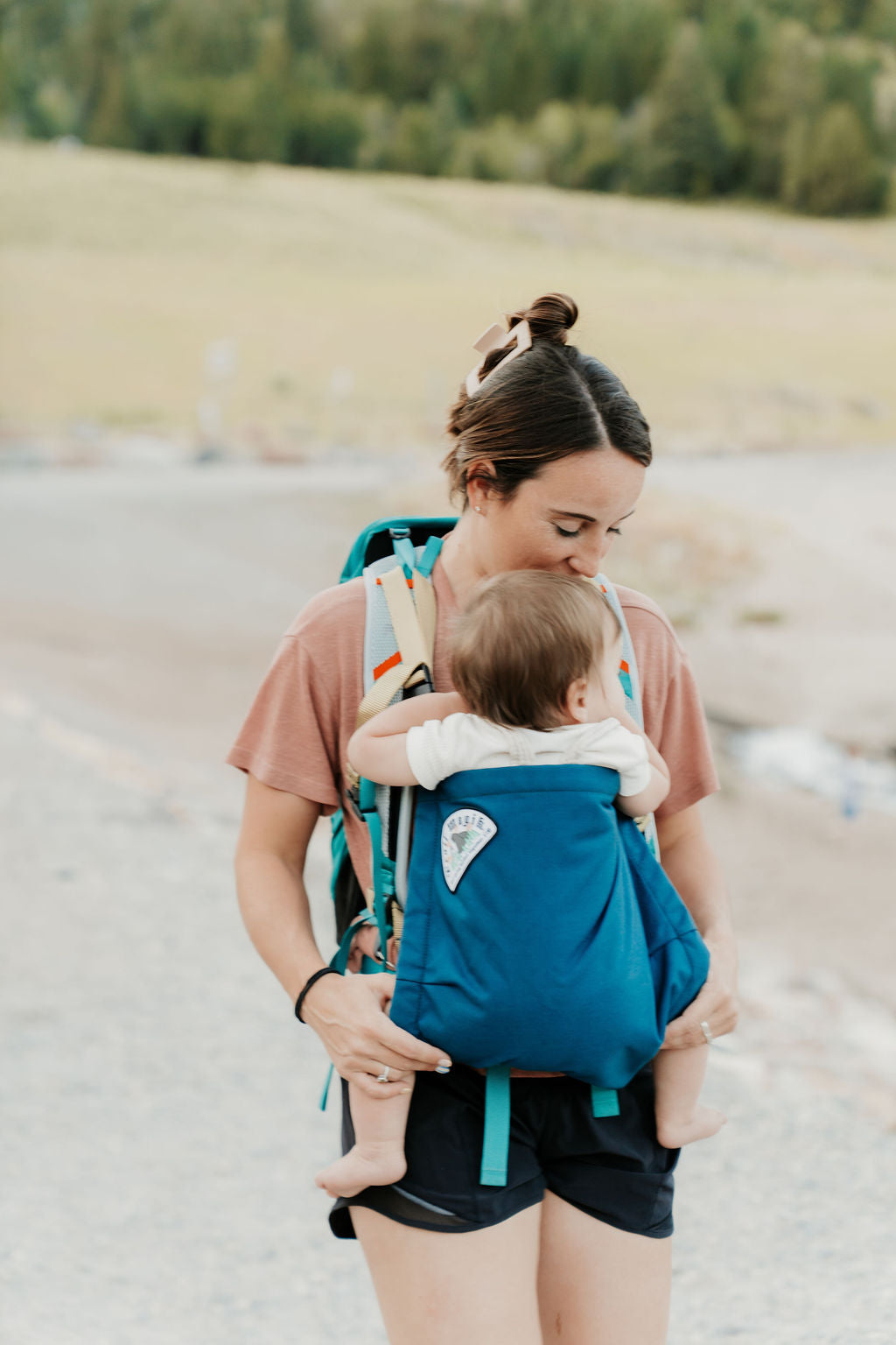 Woman carrying a child in a blue baby carrier outdoors.