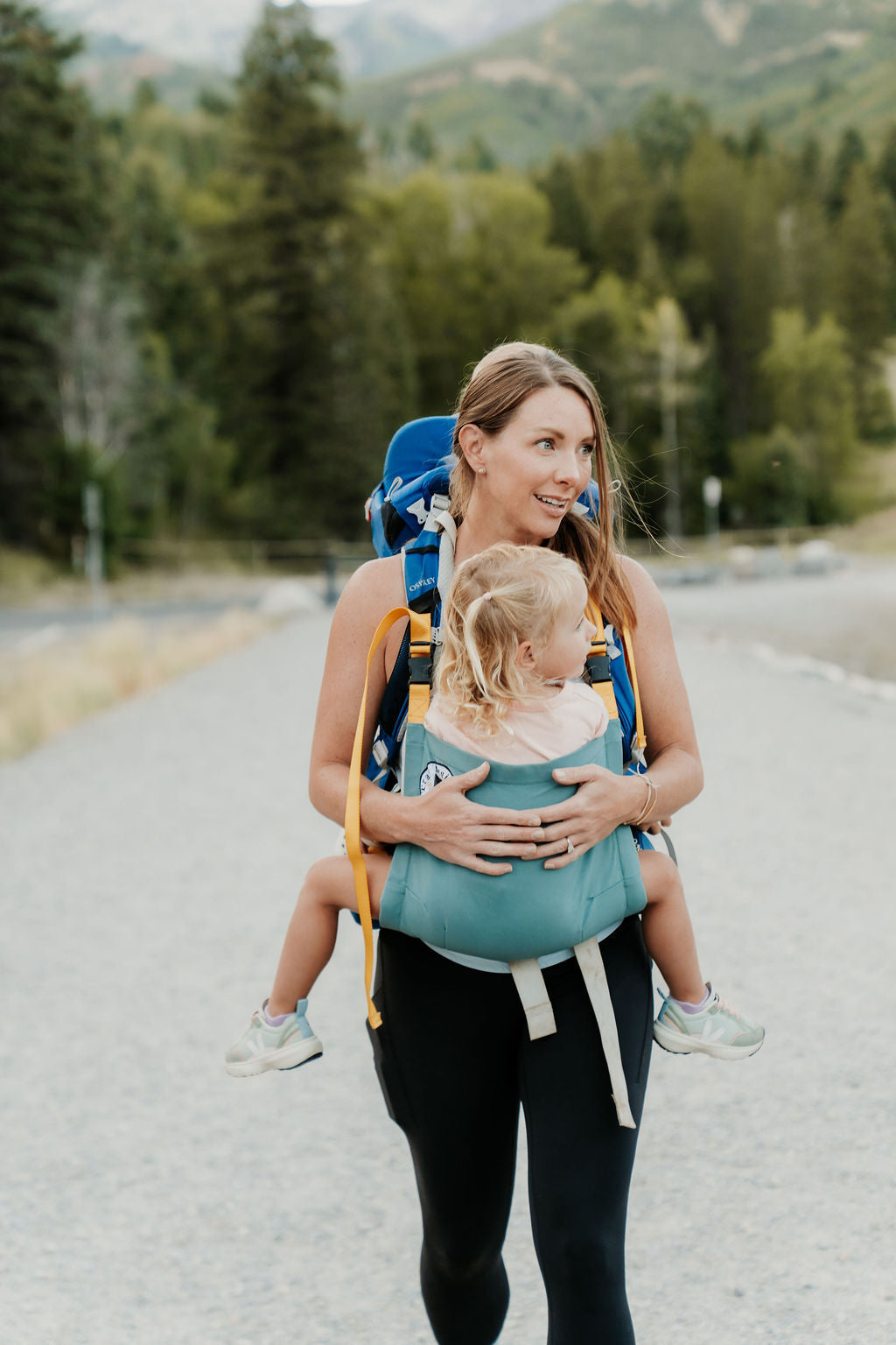 Woman walking outdoors with a child in a blue baby carrier