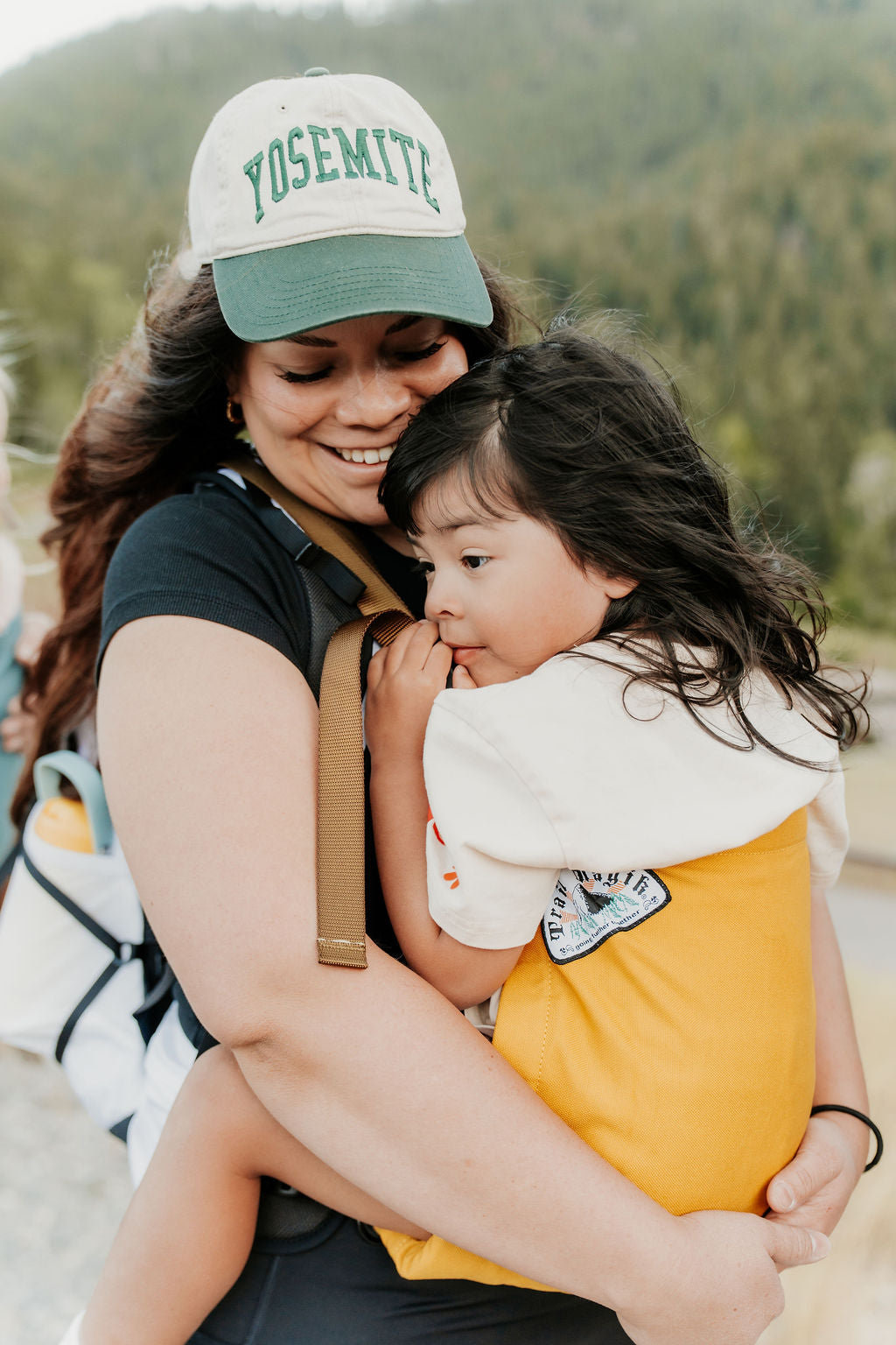 Woman holding a child with a Yosemite cap in a natural setting
