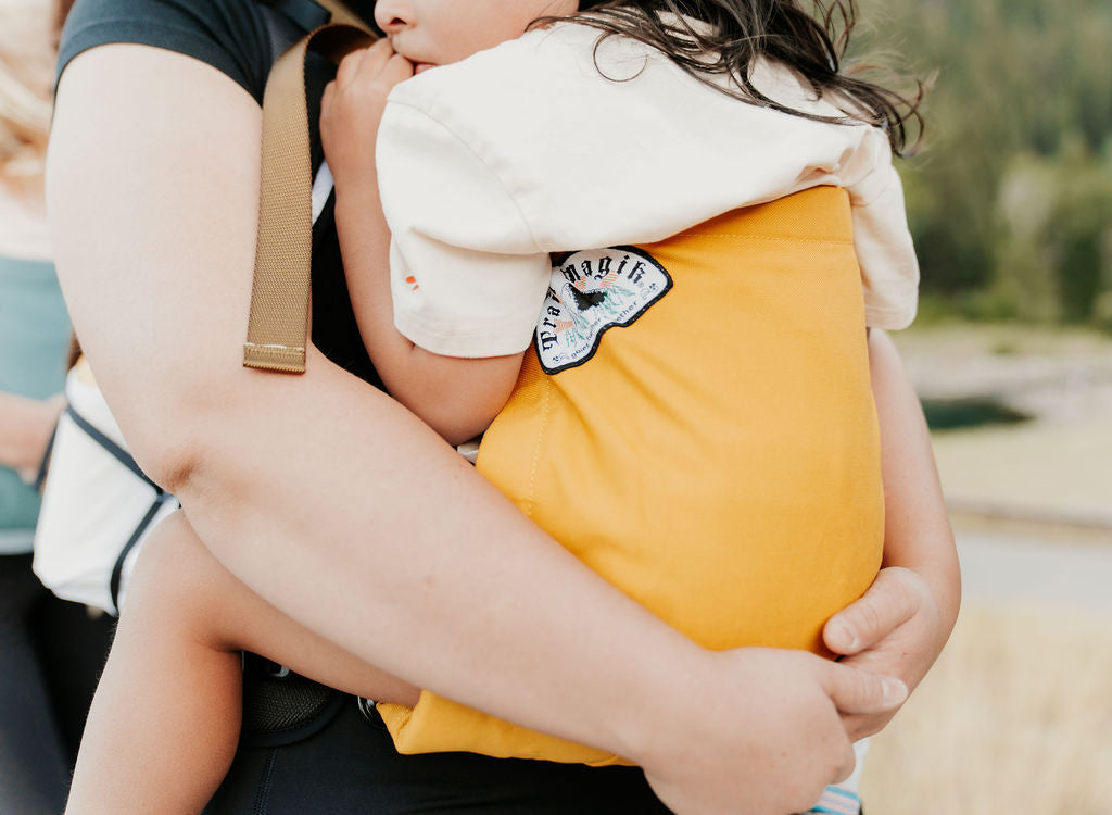 Person holding a child wearing a yellow jacket with a patch outdoors