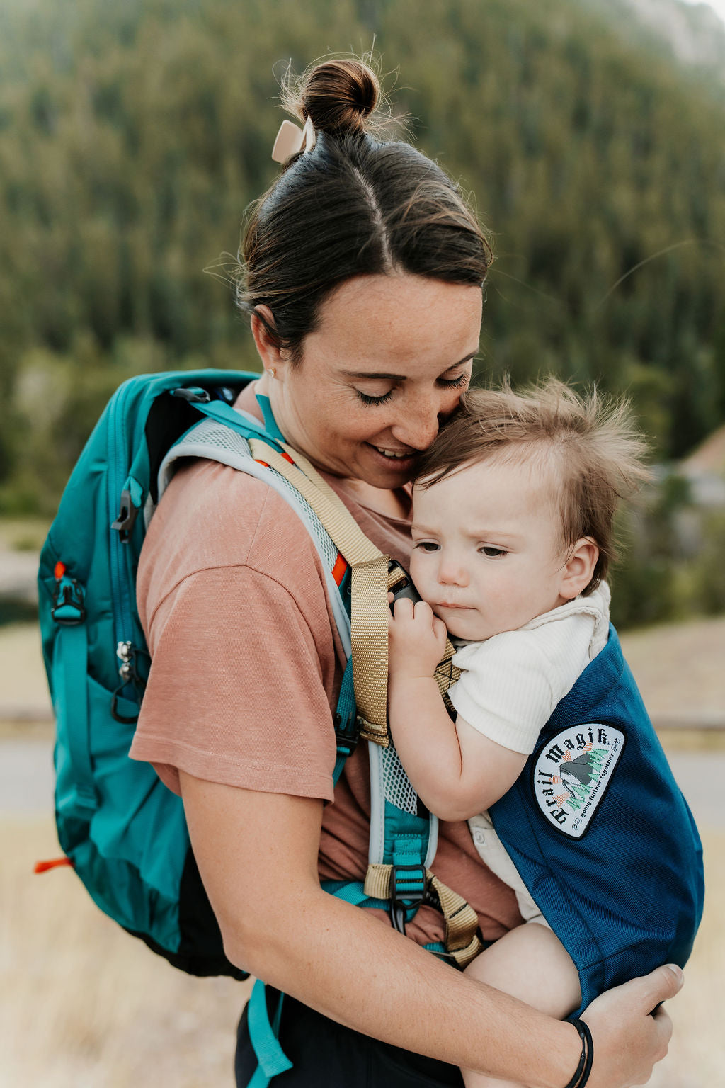 Woman carrying a child in a baby carrier with a forest in the background