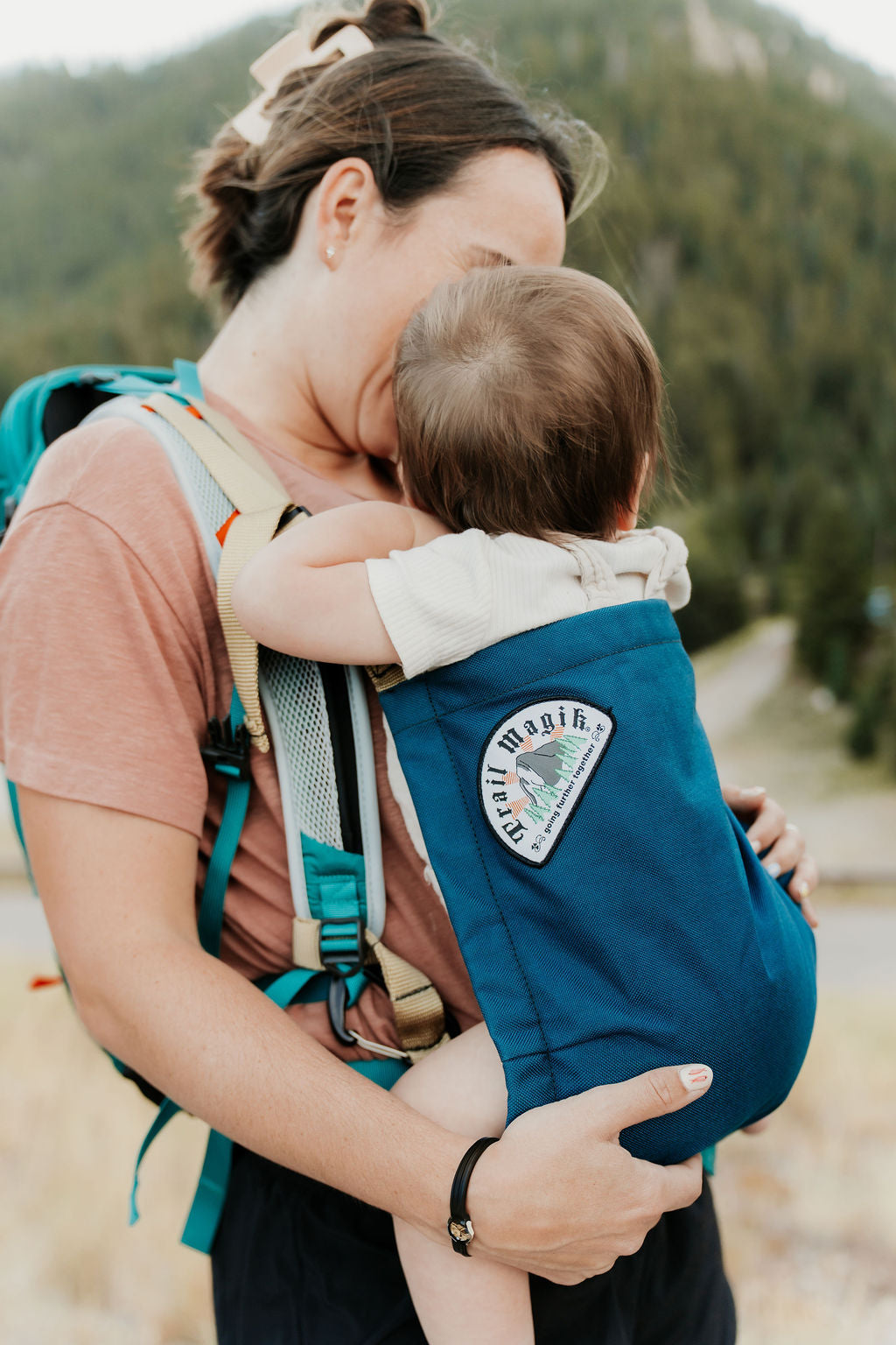 Woman carrying a child in a blue baby carrier with a scenic background