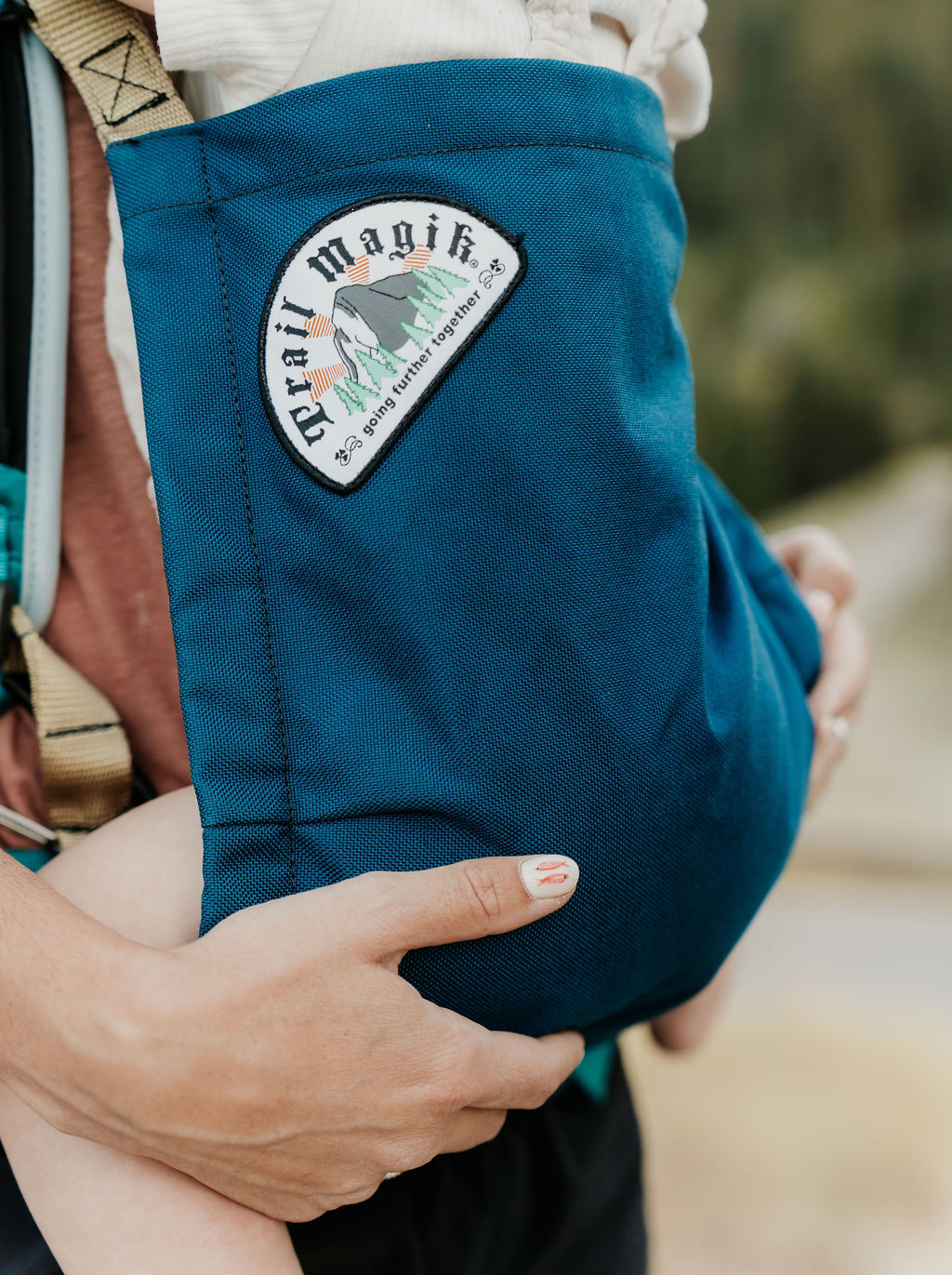 Blue baby carrier with a visible brand patch on a blurred natural background