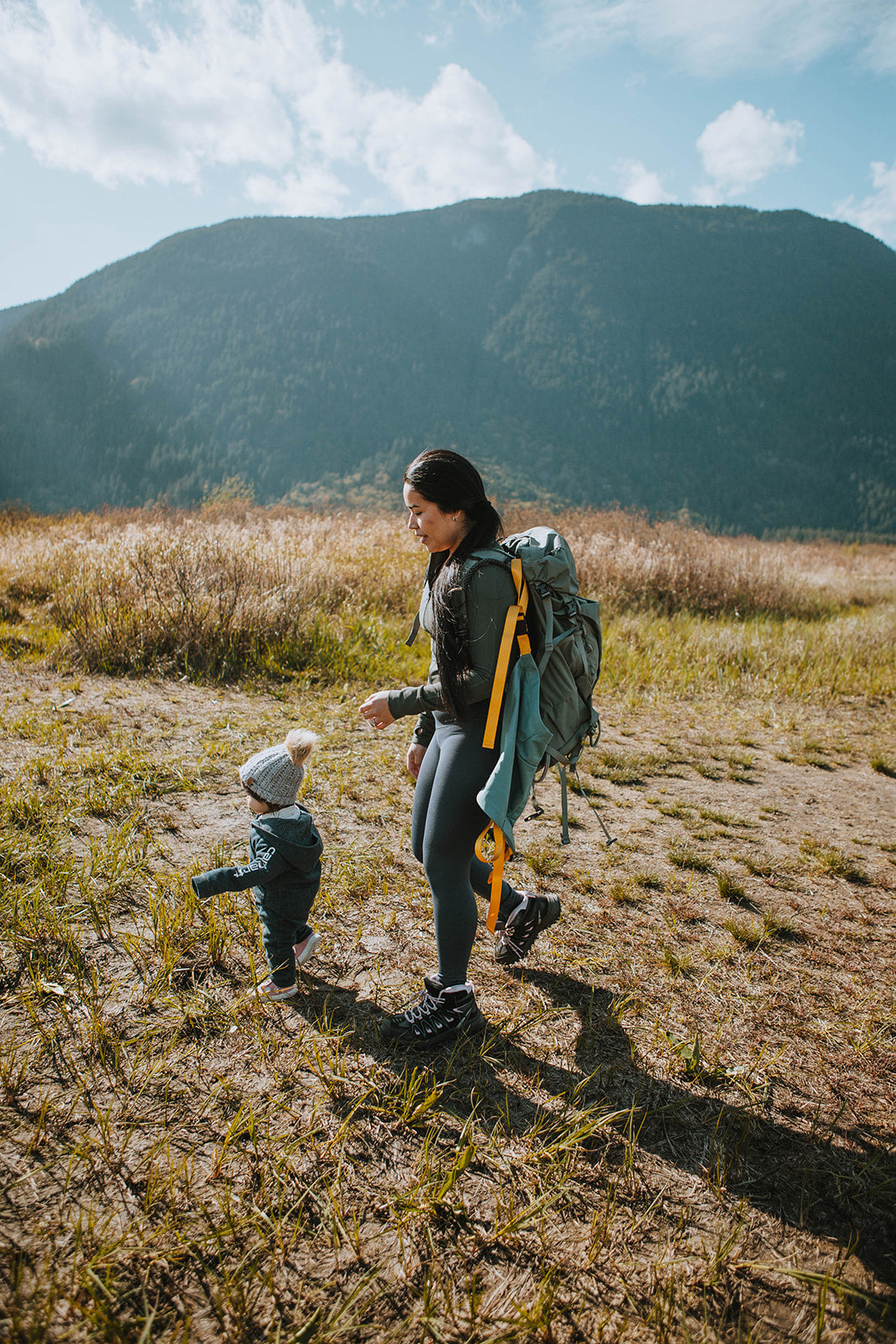 Woman with a child walking in a field with mountains in the background