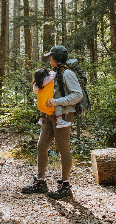 Person hiking in a forest with a child in a carrier