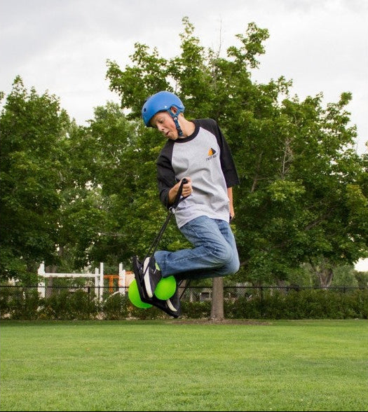 Person performing a trick on a scooter in a park with trees and grass in the background
